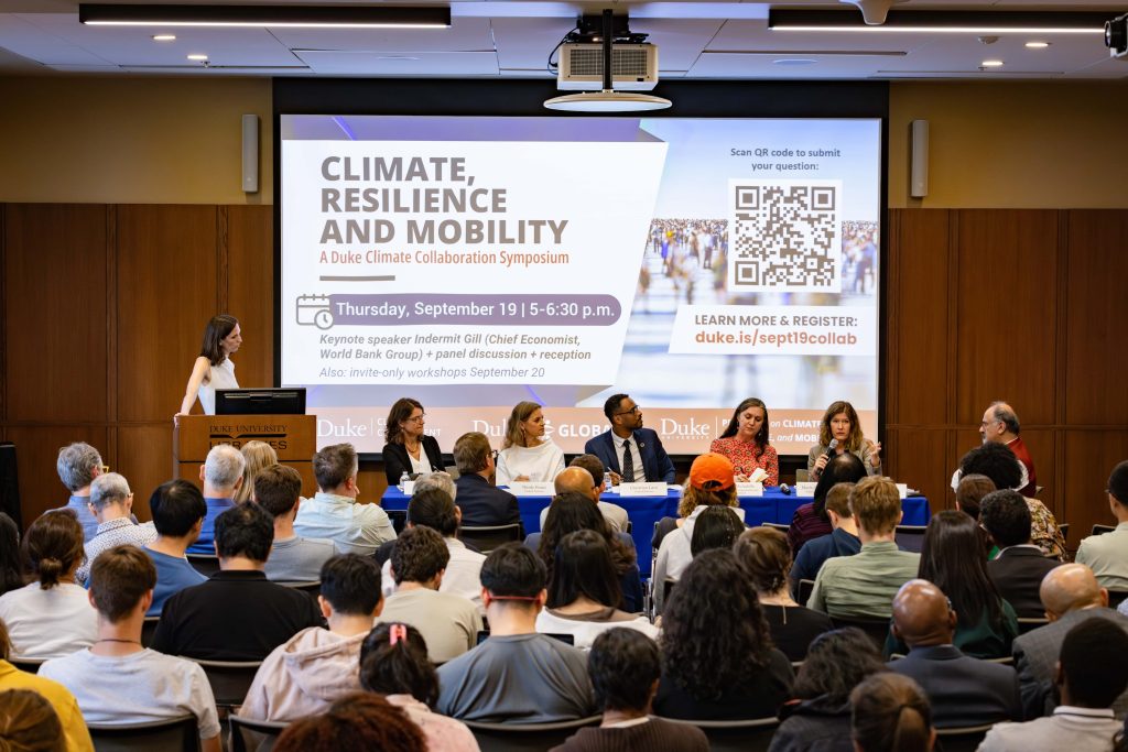 A panel of six people sit at a table in the front of a crowd and discuss climate, resilience and mobility.