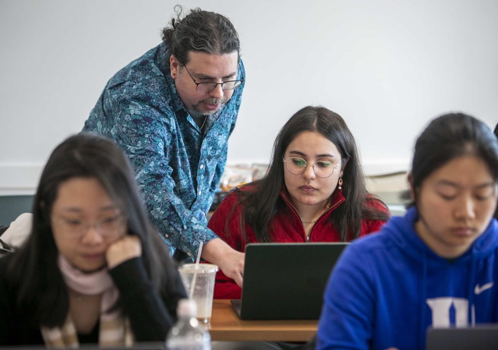 Instructor helping a student with something on their opened laptop.